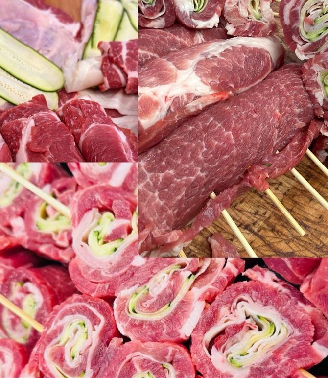 Su un vassoio si trovano diversi tagli di manzo crudo e fette di carne arrotolate, con verdure sullo sfondo.