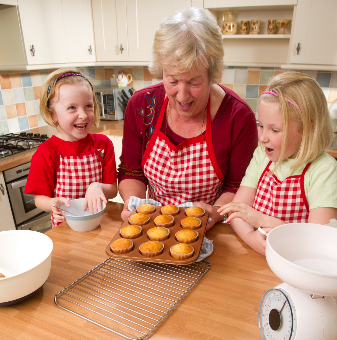 Woman and two girls in aprons admire freshly baked muffins.
