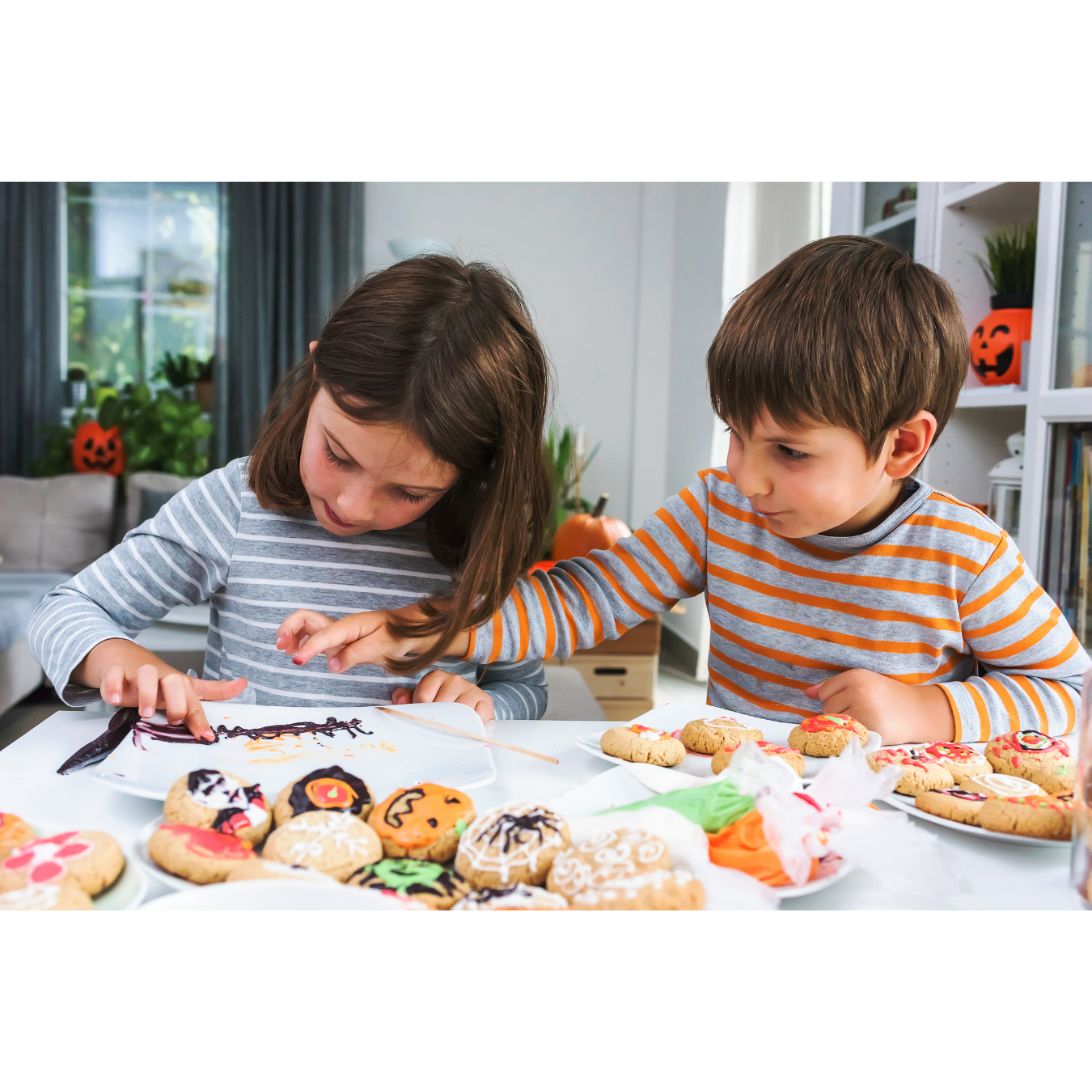 Two children decorating Halloween cookies at a table, with various decorated cookies in front of them.