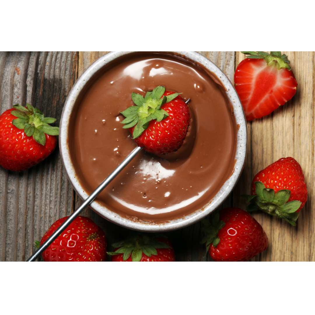 A single strawberry dipped into a bowl of melted chocolate, surrounded by fresh strawberries on a wooden surface.