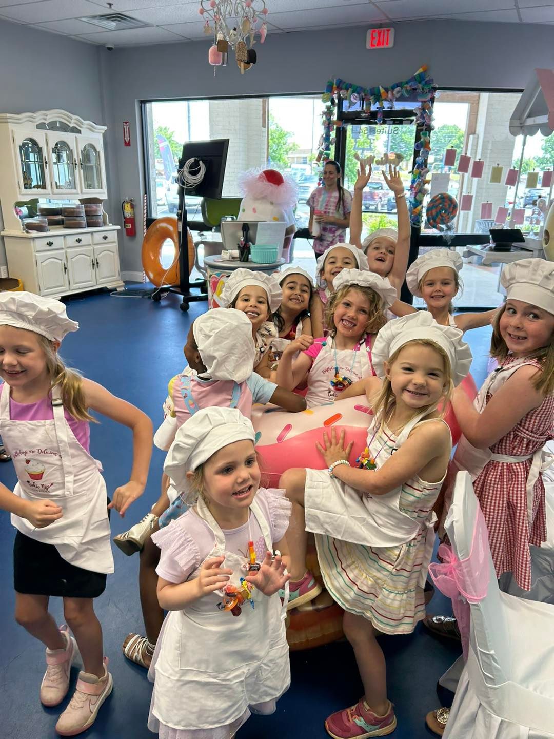 A group of children in chef hats and aprons pose in a brightly lit bakery-themed play area.