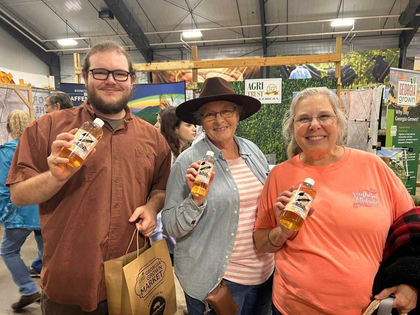 Three people hold small plastic bottles of Cookie Nip while standing in a booth at an indoor market.