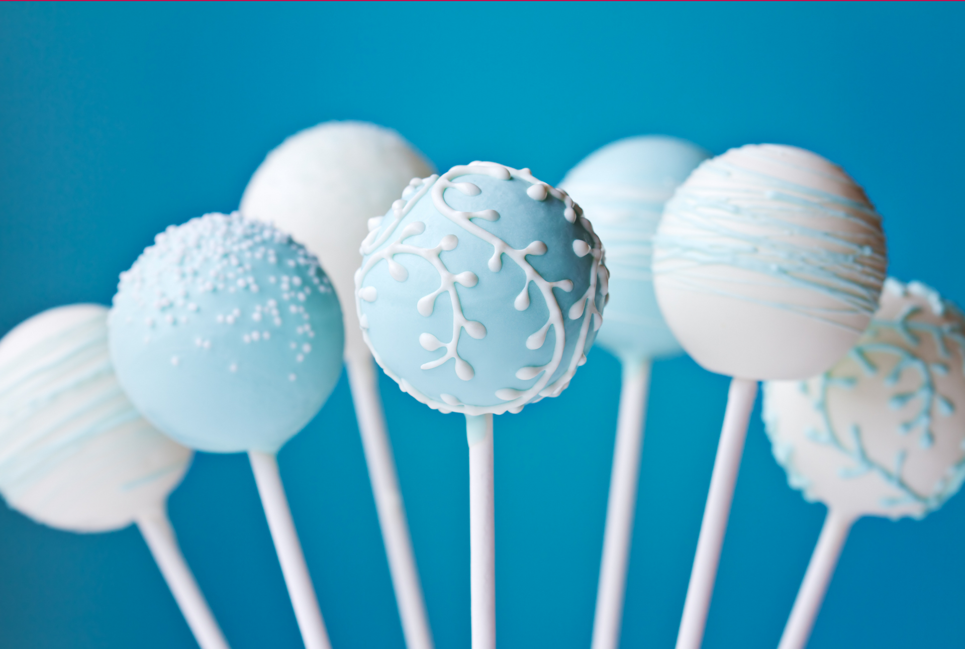 Seven cake pops decorated in shades of blue and white, arranged against a solid blue background.