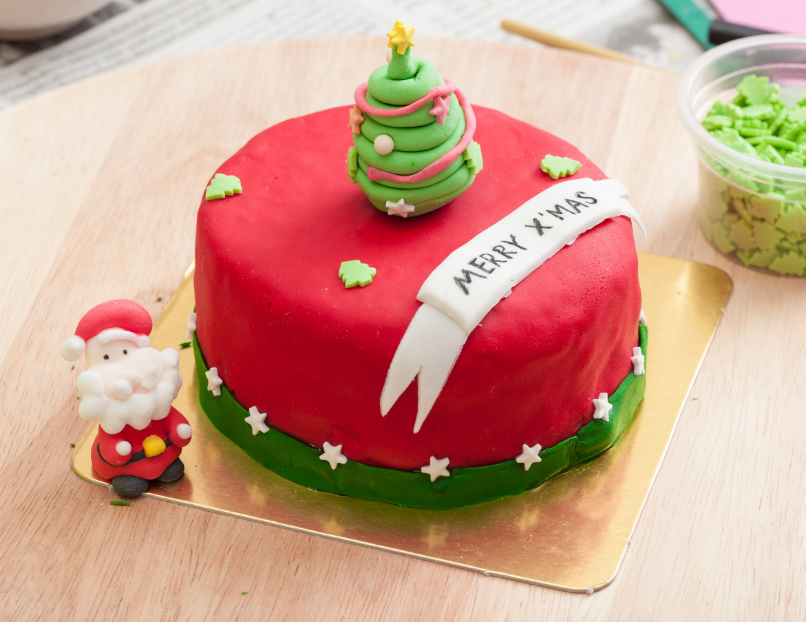 A red-frosted Christmas cake topped with a small tree figurine, a 