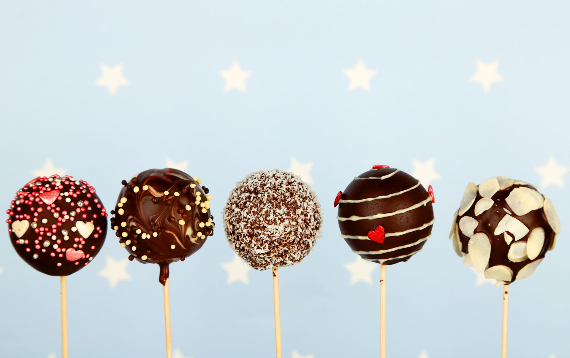 Five chocolate cake pops with various toppings, arranged in a row against a light blue background with white star patterns.