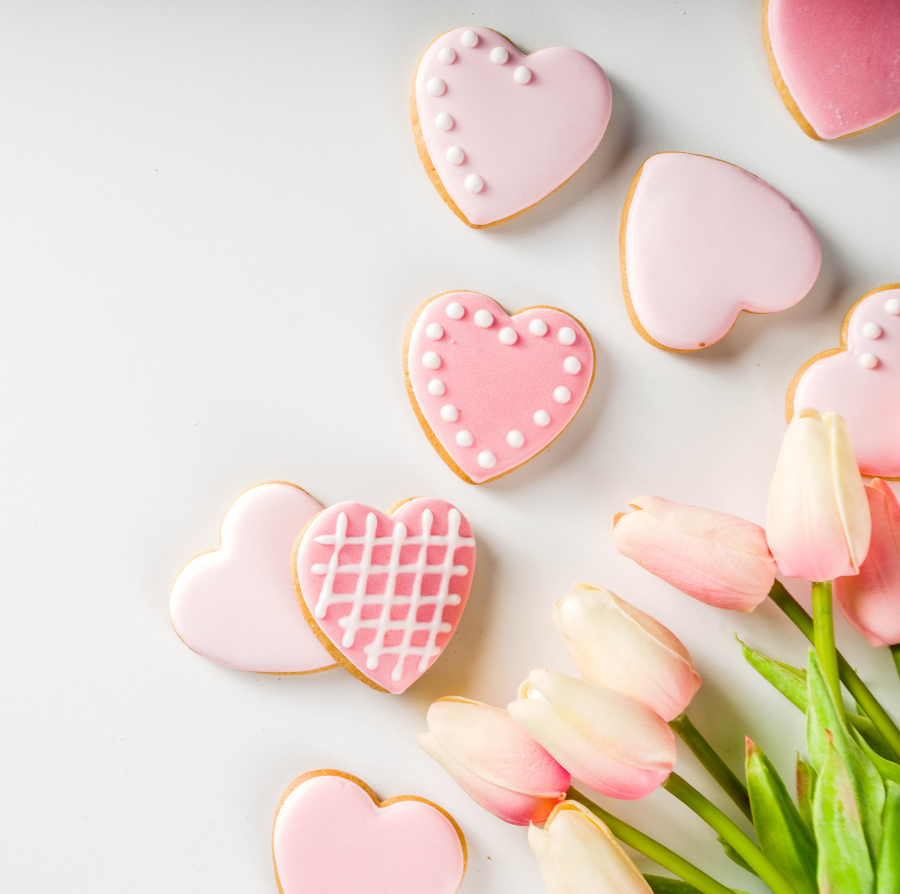 Pink heart-shaped frosted cookies and a bouquet of soft pink tulips arranged on a clean, light-colored background.