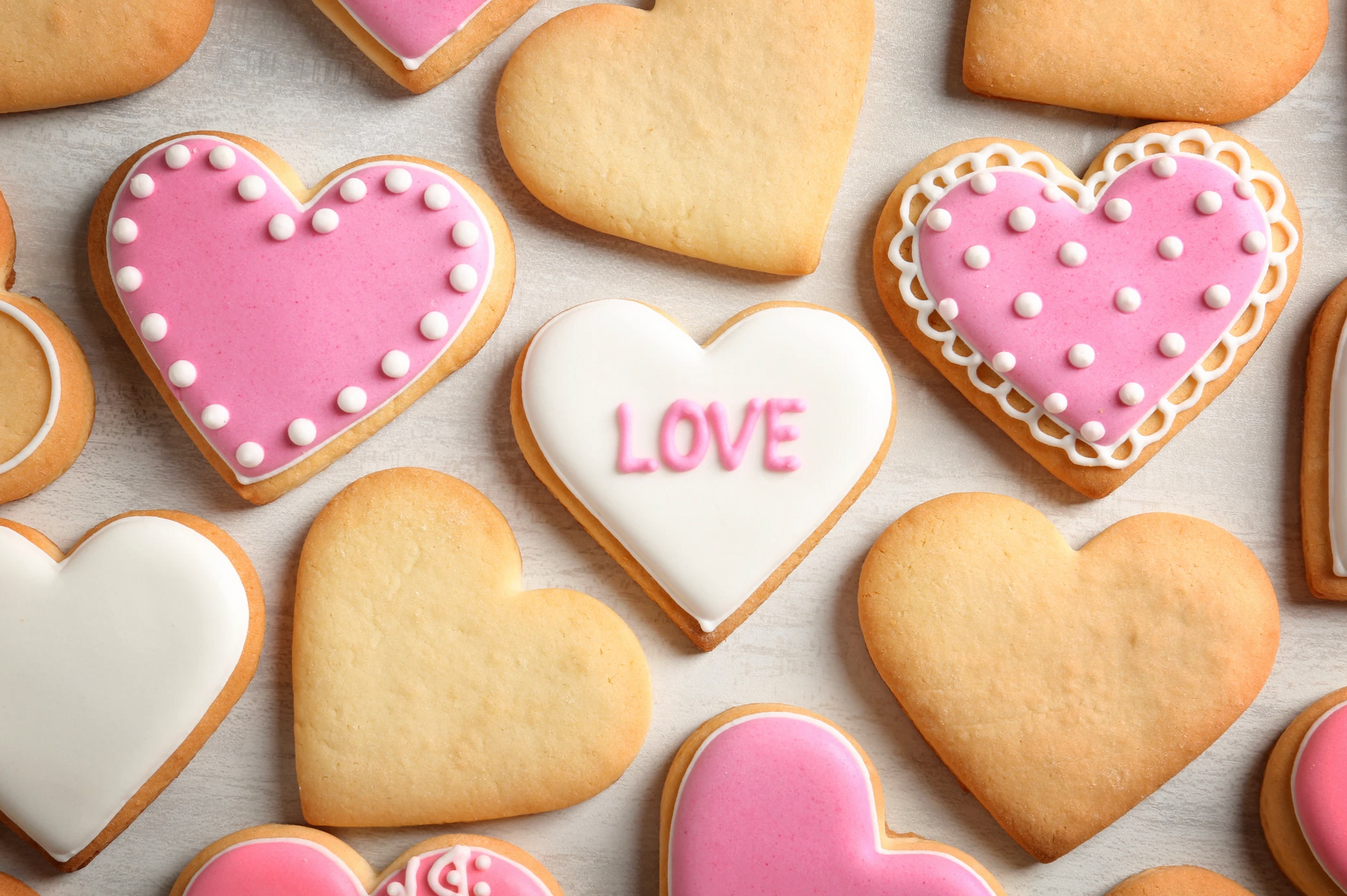A collection of heart-shaped sugar cookies, some decorated with pink frosting or white text reading 