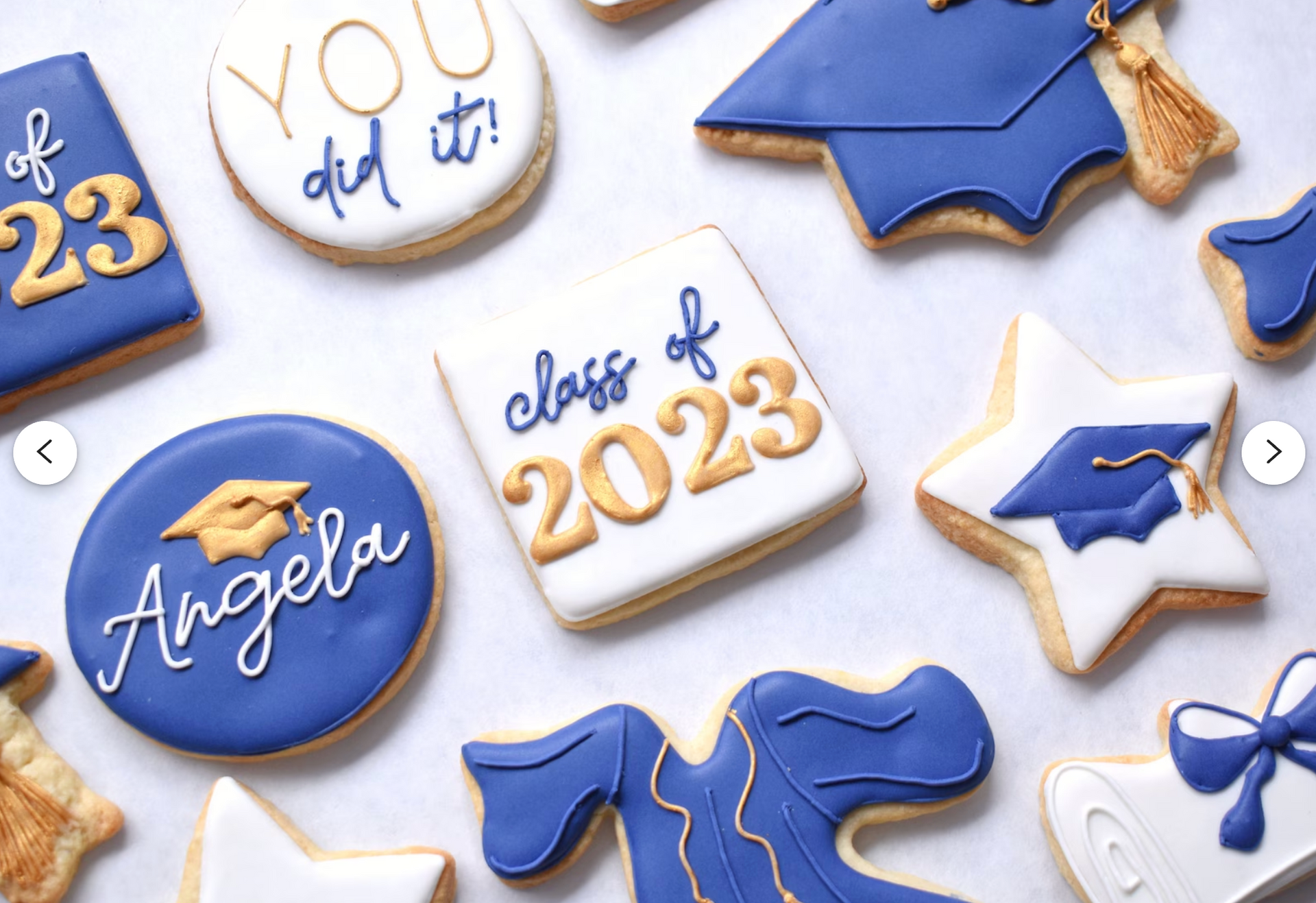 A flat lay of graduation-themed cookies in blue, white, and gold, featuring mortarboards, star shapes, and text.