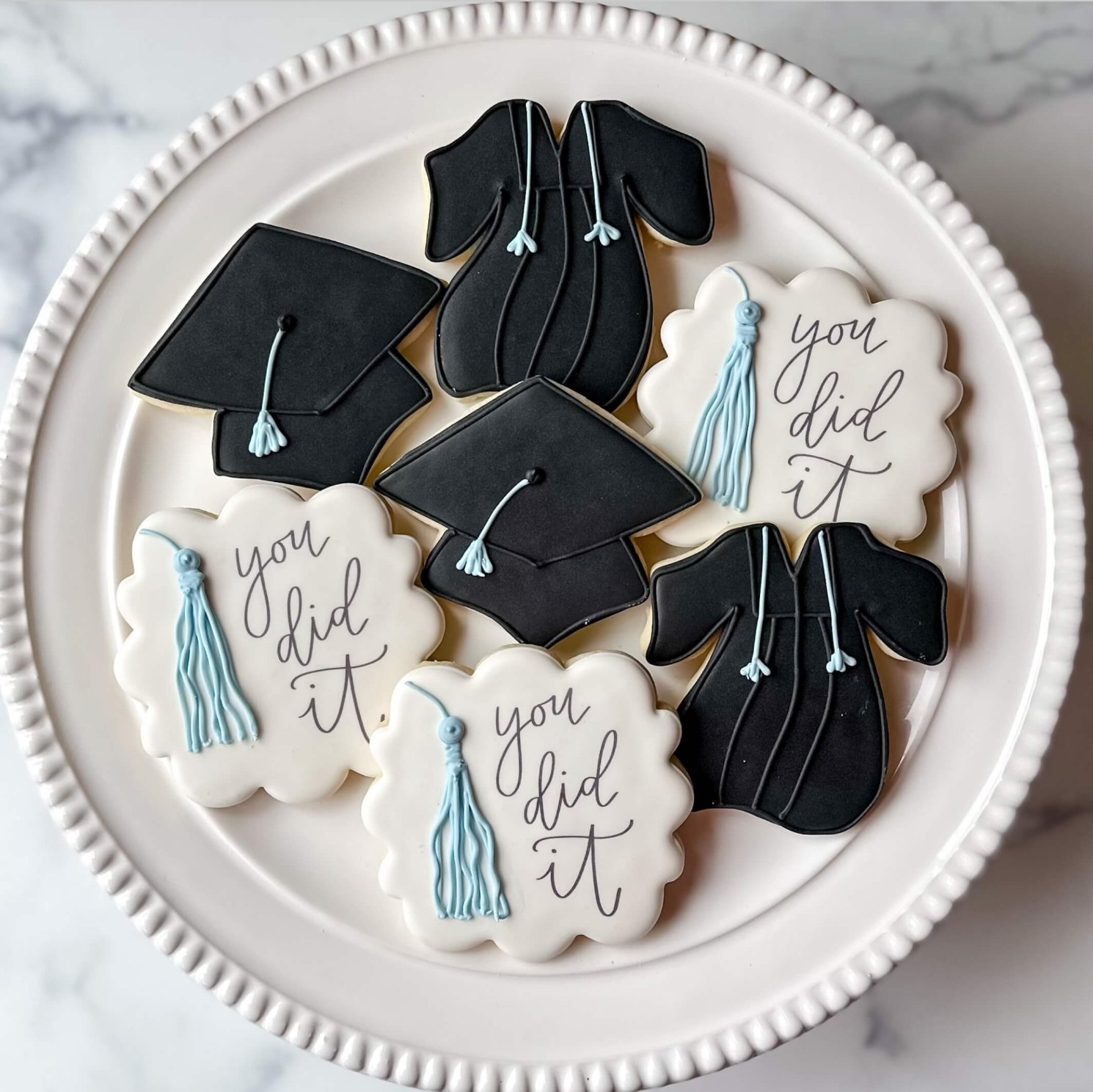 Graduation cookies on a white plate: black caps, black gowns, and white plaques with 