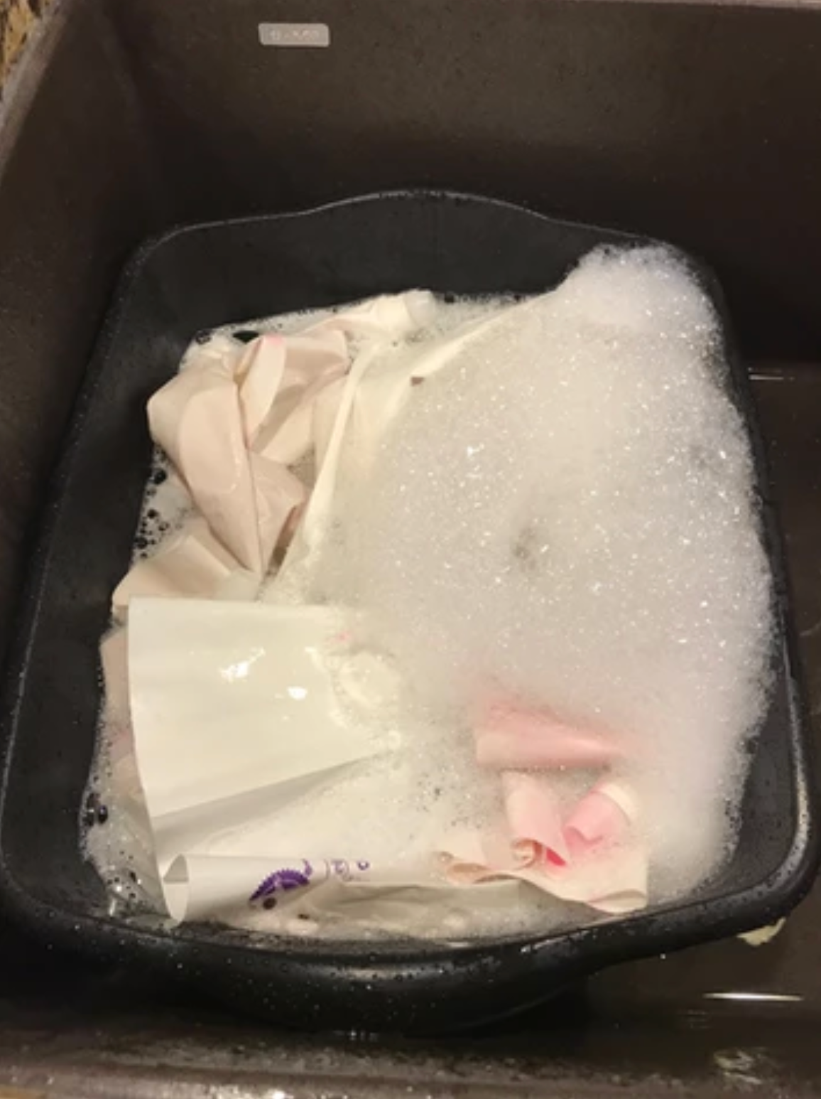 Laundry in a black basin filled with soapy water. White and pink fabric submerged in bubbles.