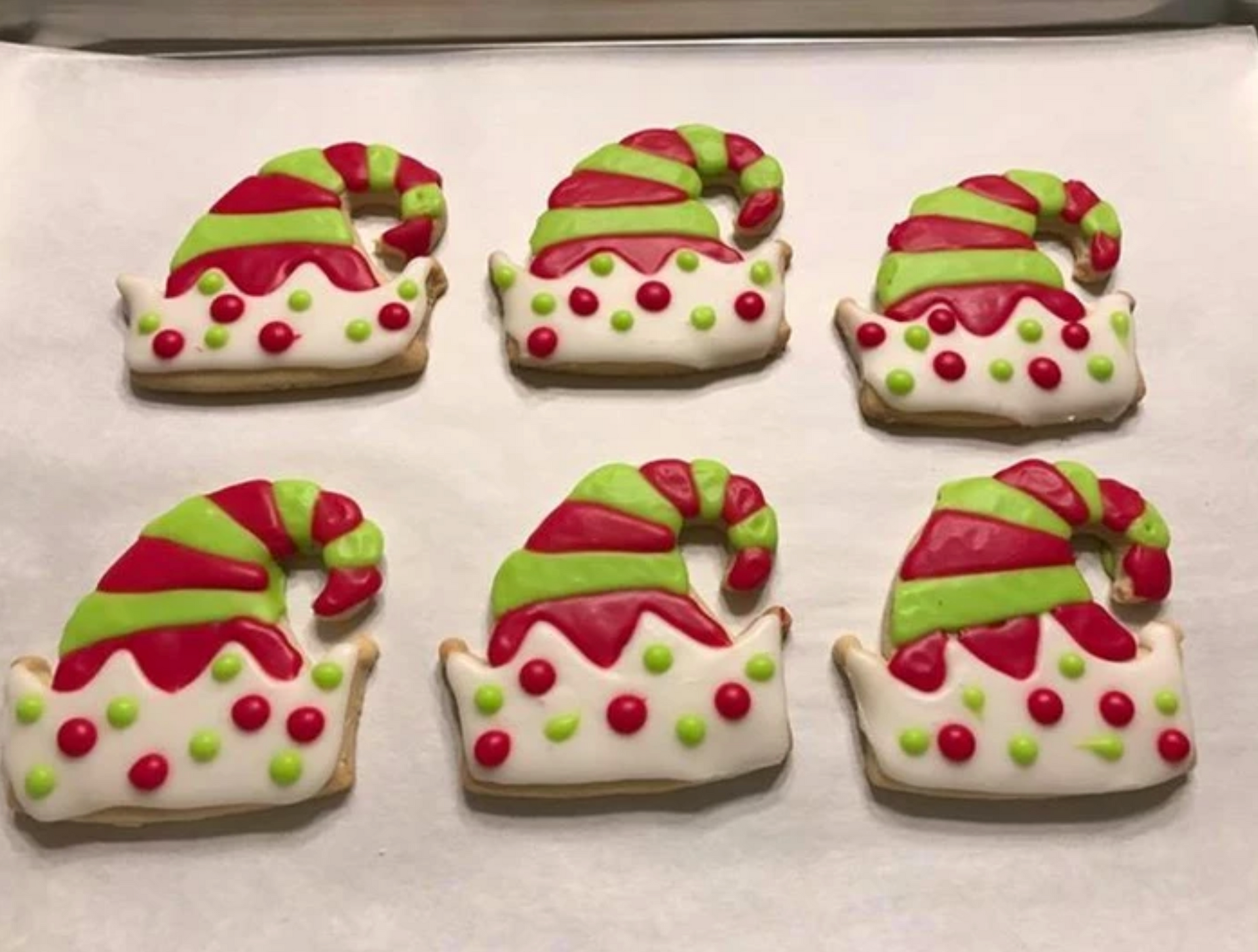 Six elf hat-shaped sugar cookies with red, green, and white icing on parchment paper.