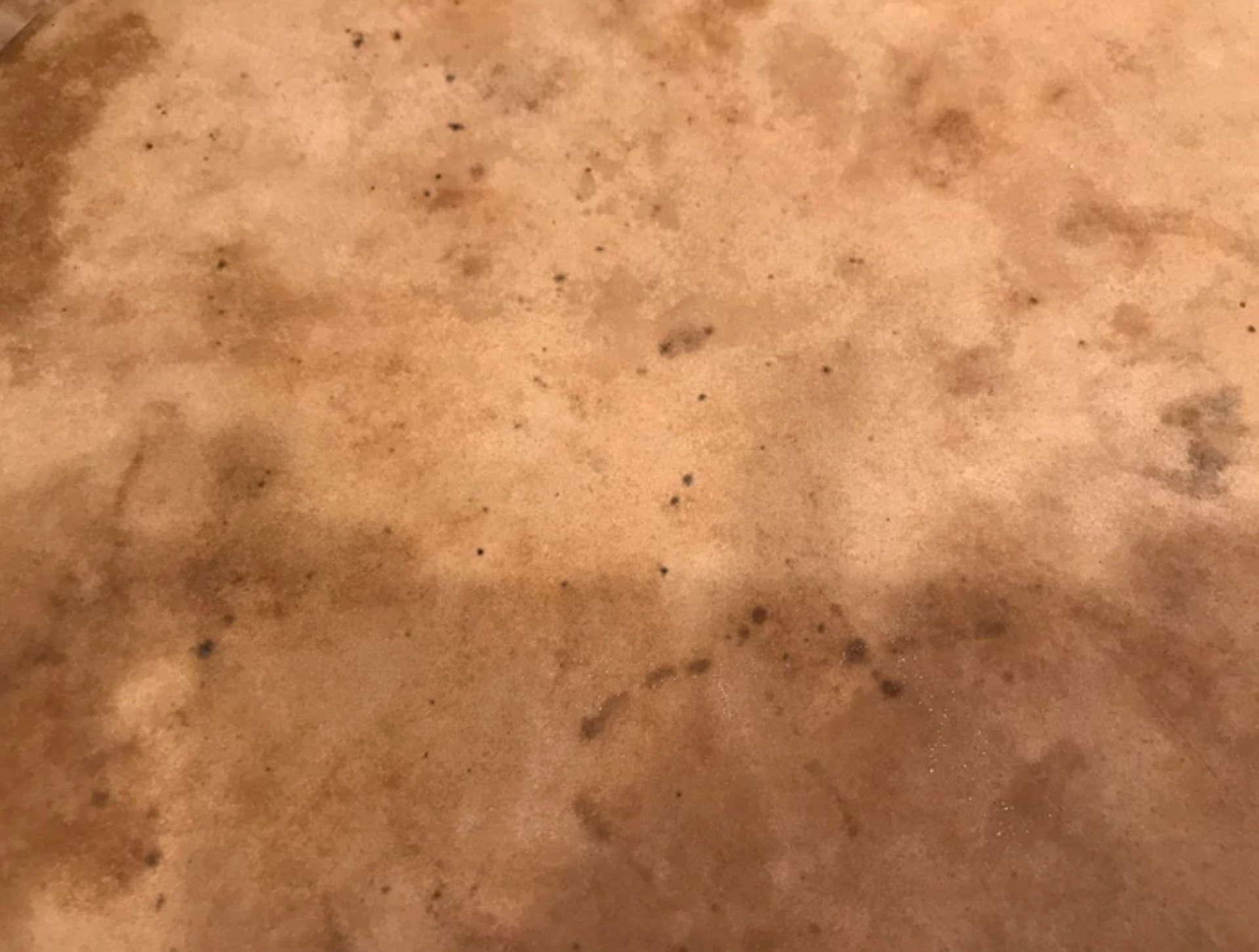 Close-up of a stained tan surface with dark brown spots and areas of discoloration.