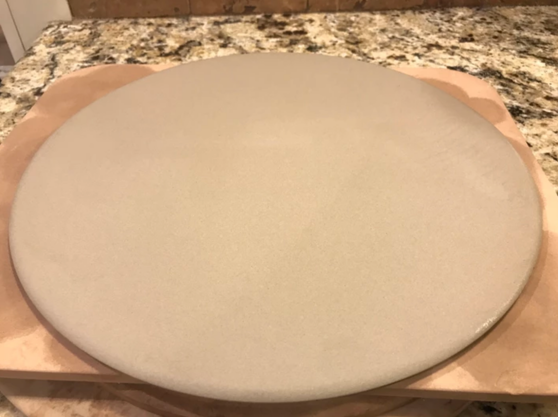 Round pizza stone on a wooden peel, set against a speckled countertop.