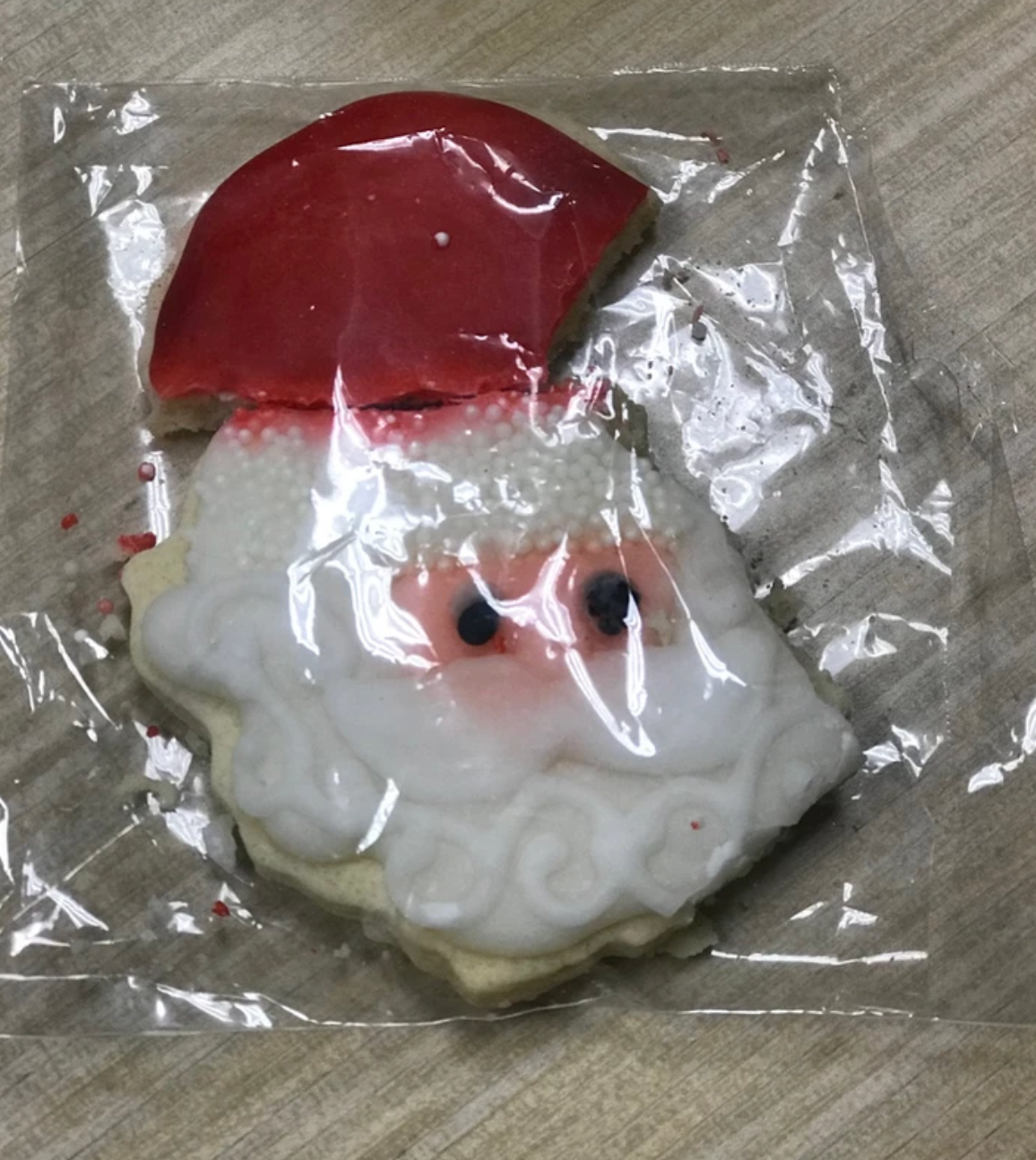 Santa cookie in clear plastic wrapper, red hat, white beard, pink cheeks.