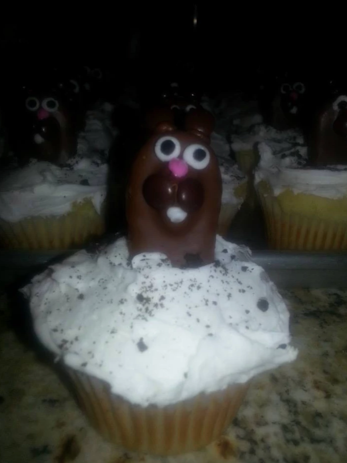 Cupcake with white frosting, chocolate bunny candy on top; other cupcakes in background.