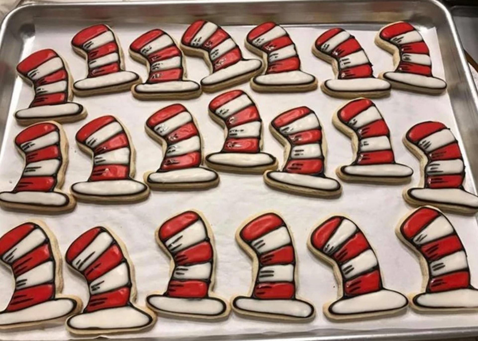 Cat in the Hat hat-shaped cookies on a tray, with red and white stripes and black outlines.
