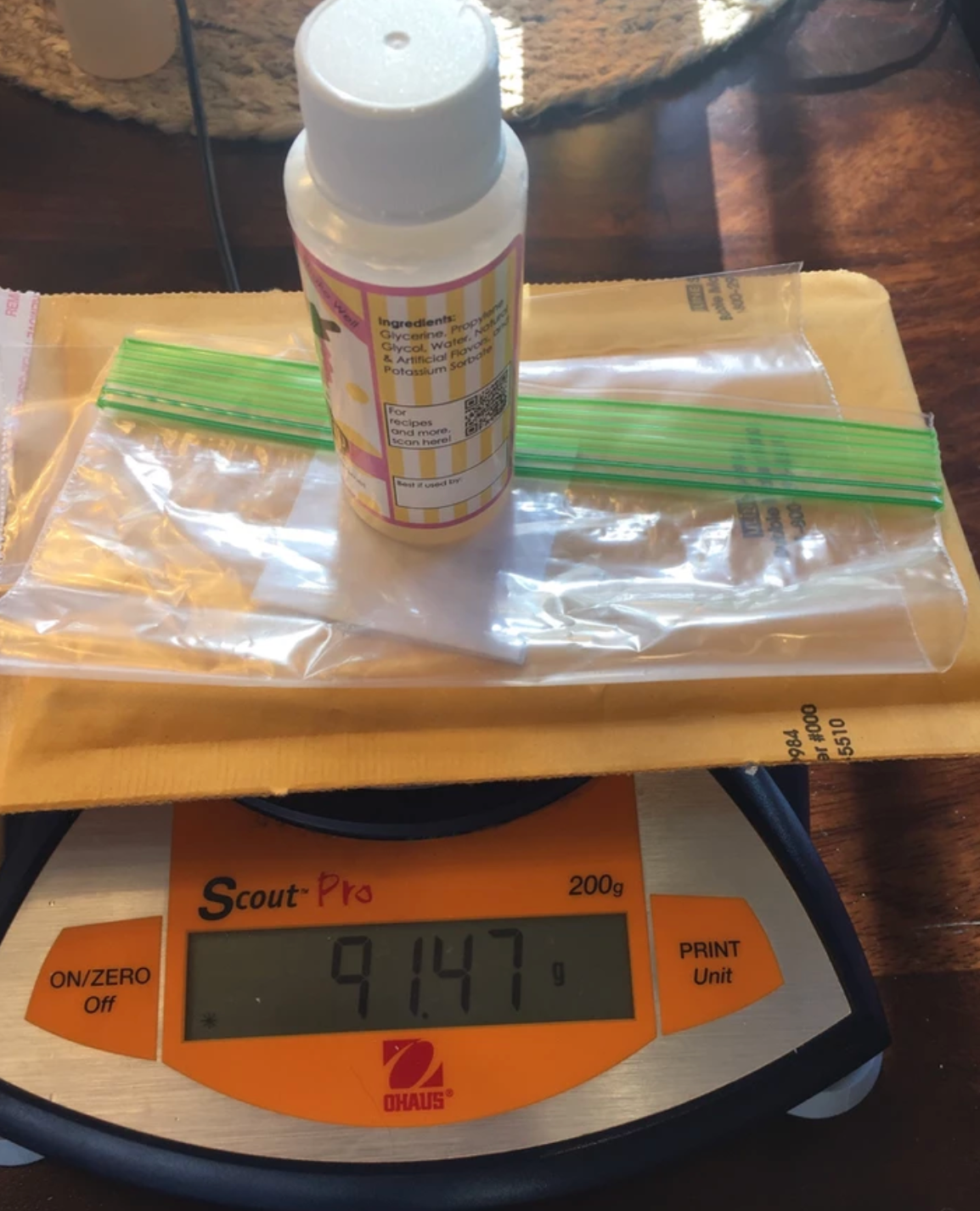 A bottle, two plastic bags, and an envelope are on a scale; it reads 914.7.
