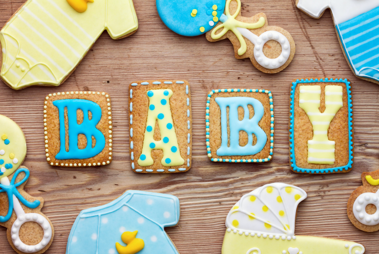 Cookies shaped as baby items and the letters B-A-B-Y are arranged on a wooden surface.