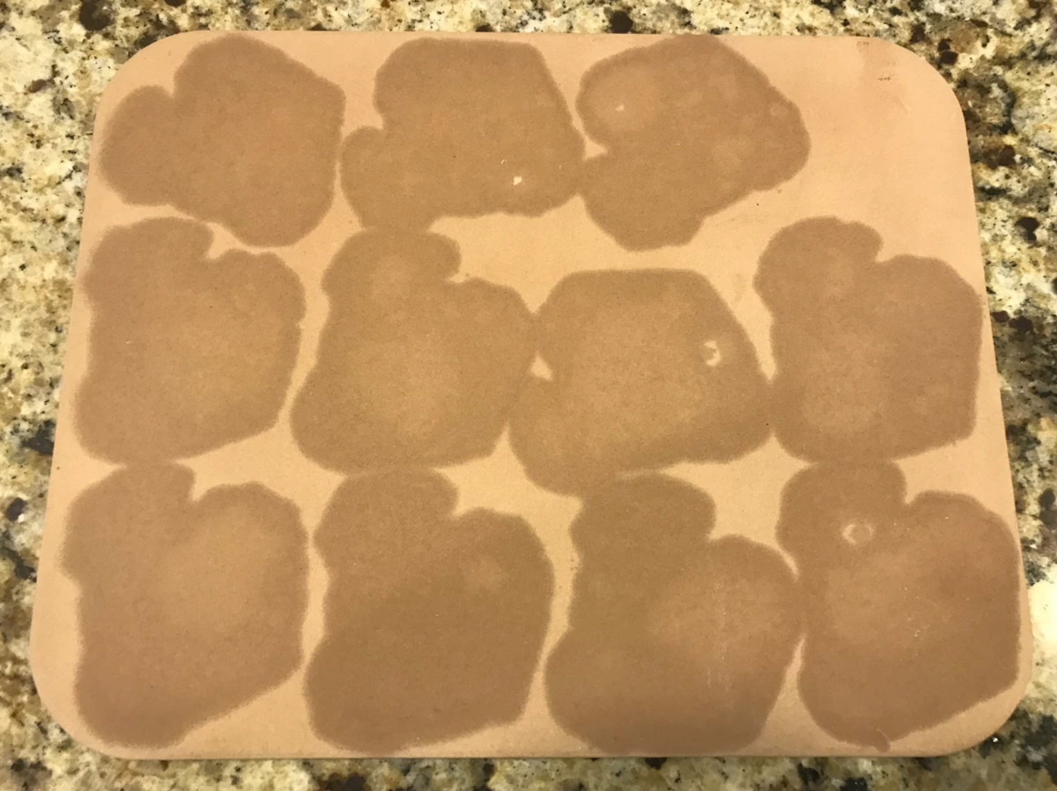 Brown square cutting board with 12 wet marks in a grid pattern.