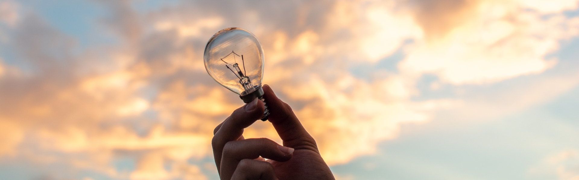Hand holding a lightbulb against a cloudy sky, suggesting an idea or inspiration.