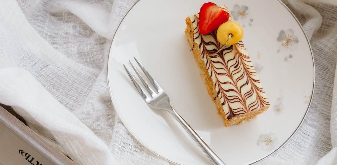 A single mille-feuille pastry topped with a strawberry and a golden berry on a floral plate with a fork, on a white cloth.