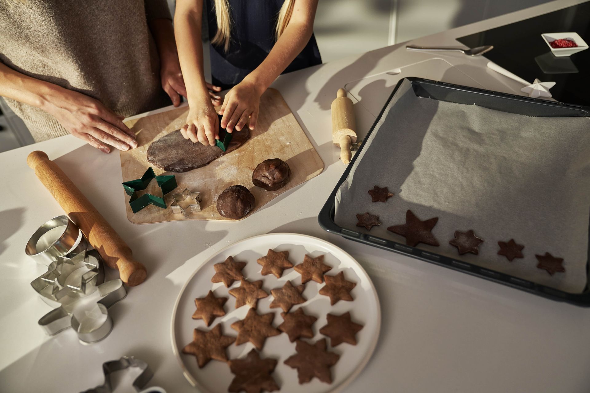 Cookies being made: hands cutting dough on a board, star-shaped cookies on a plate and baking sheet.