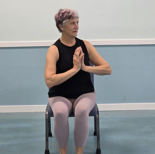 Woman seated on a chair, hands together in a yoga pose in a studio room