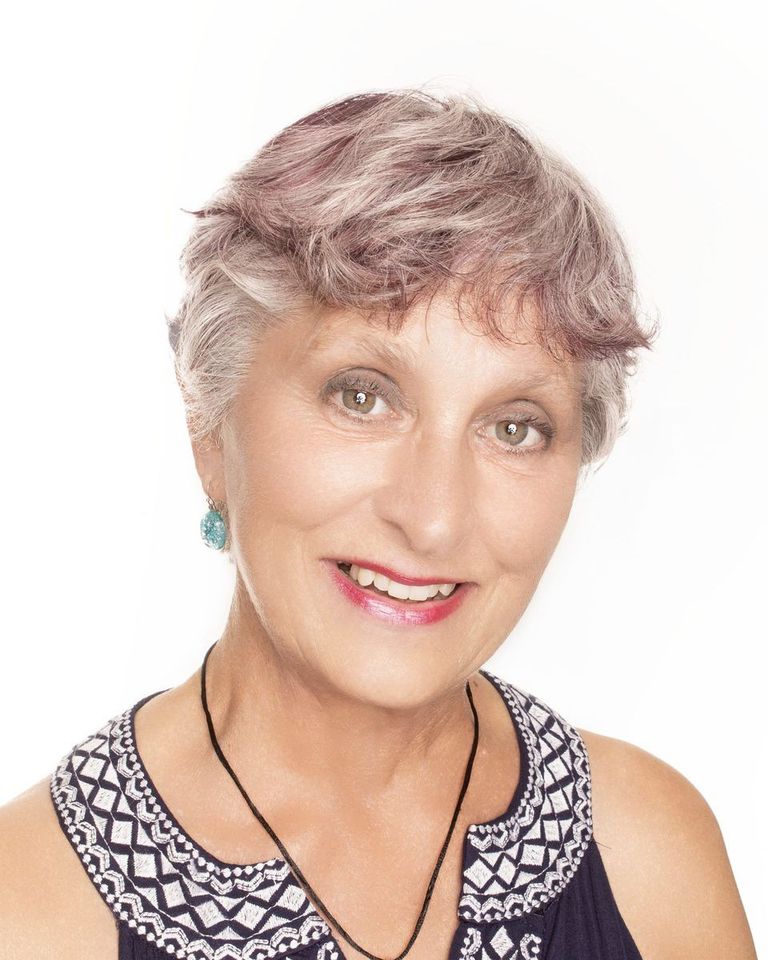 Portrait of a smiling woman with short gray hair in a patterned sleeveless top on a white background