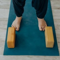 Feet standing on a blue mat beside two wooden yoga blocks.