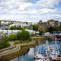 Harborfront cityscape with apartment buildings, trees, and boats on a calm marina under a cloudy sky