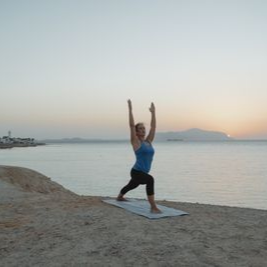 Person doing yoga pose on a mat by the sea at sunset