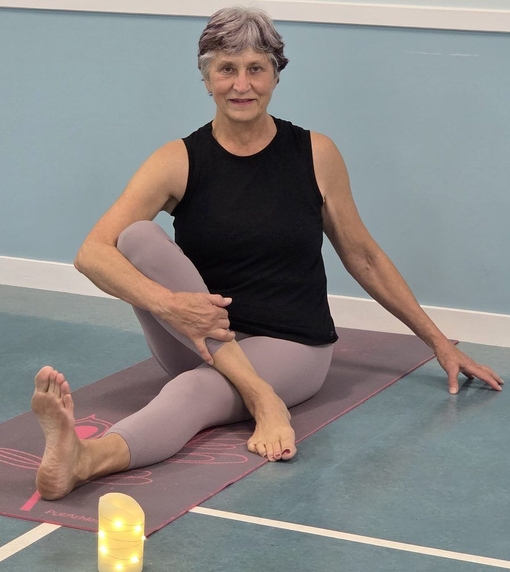 Person standing in yoga tree pose with hands in prayer, wearing black top and light leggings.
