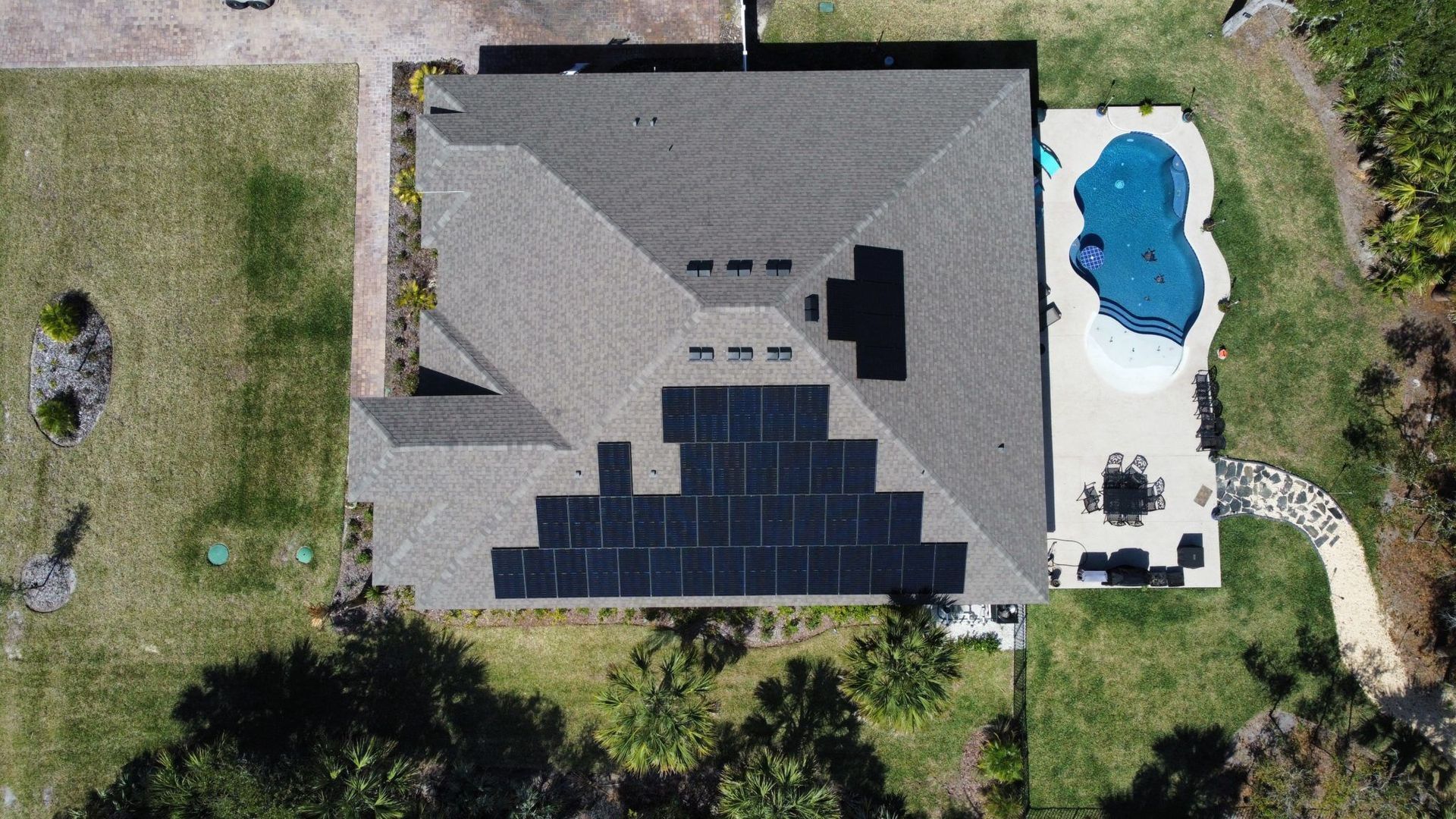 An aerial view of a house with solar panels on the roof and a pool.