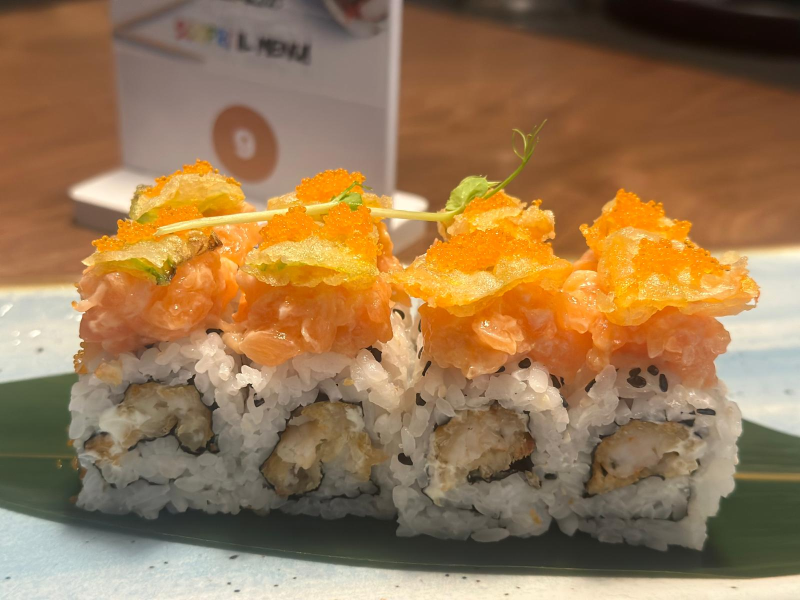 Rotolo di sushi con tempura, salmone e uova d'arancia su un piatto blu.