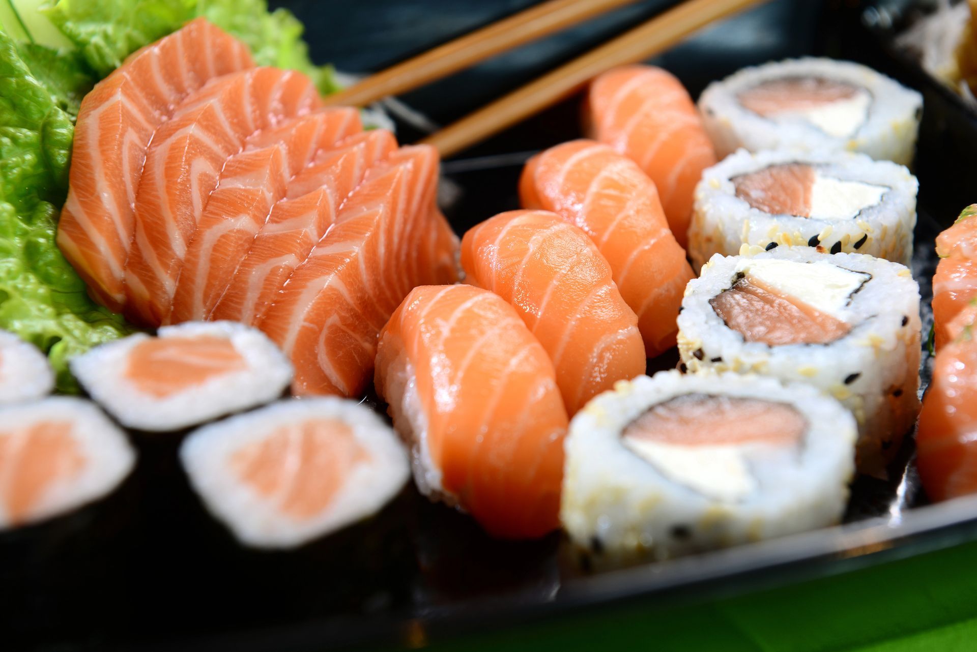Piatto di sushi e sashimi di salmone su un piatto nero con bacchette.