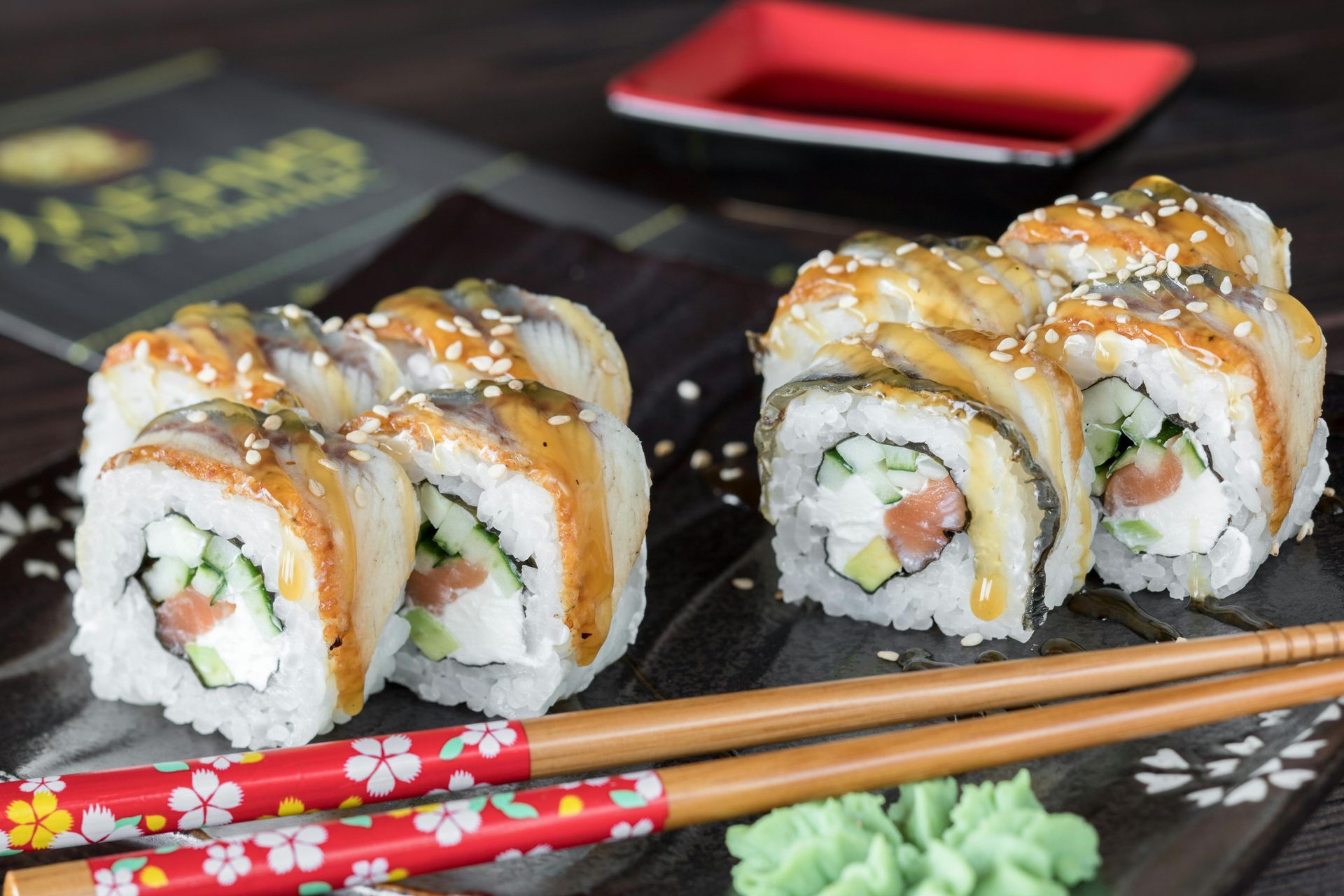 Involtini di sushi con anguilla, cetriolo e salmone, serviti con bacchette e salsa di soia.