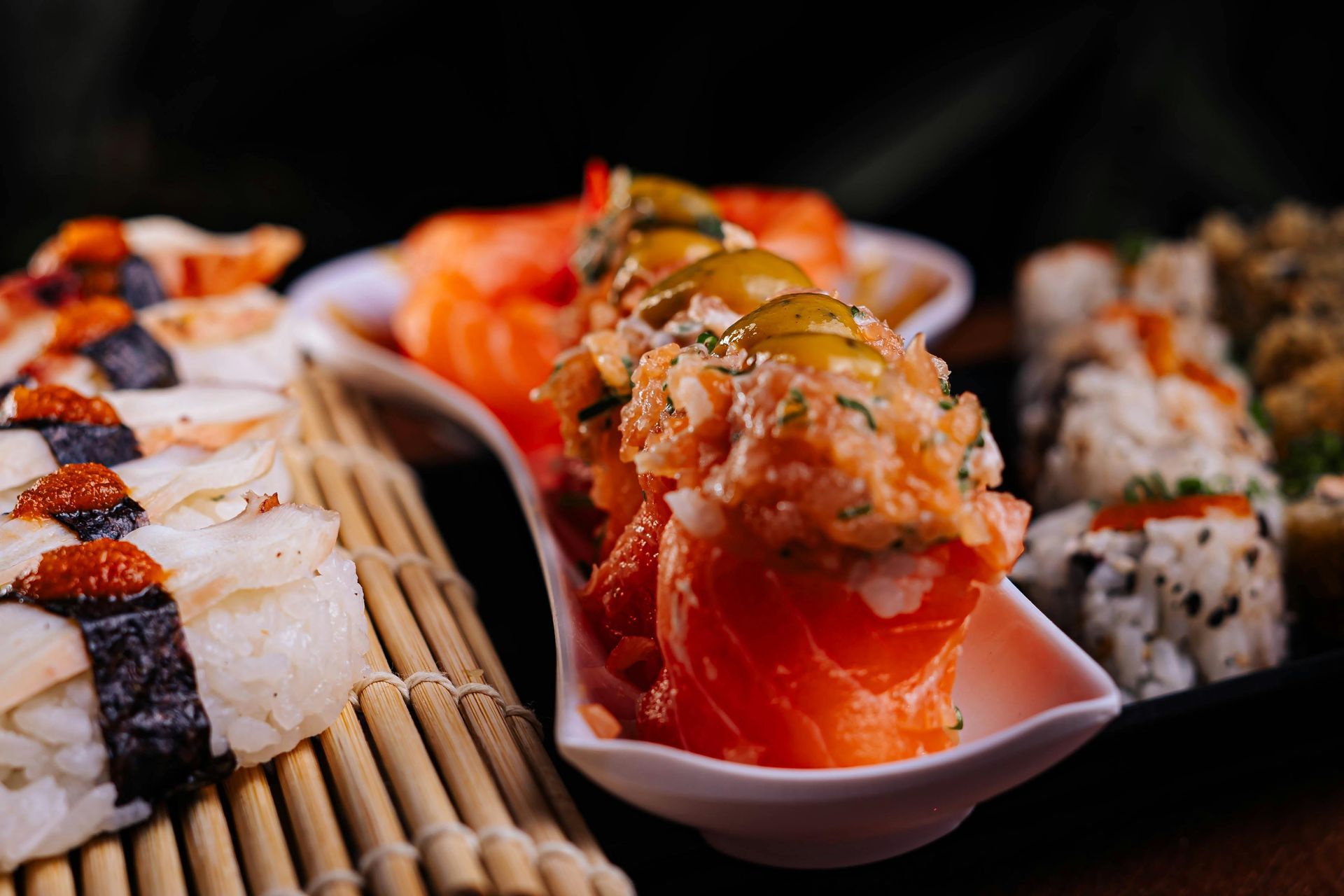 Rotoli di sushi e nigiri su stuoia di bambù, vari colori e condimenti.