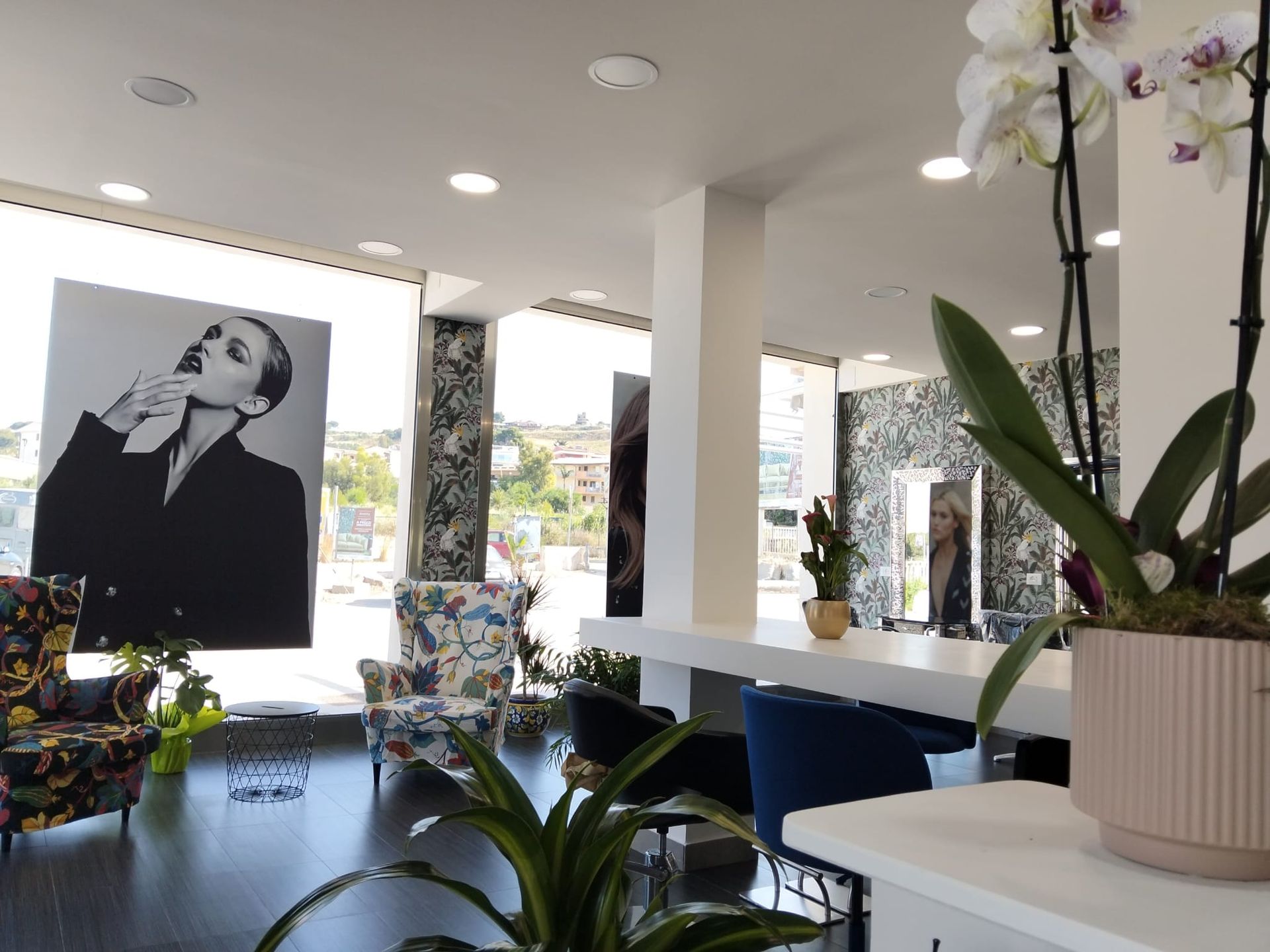 Interno moderno di una caffetteria con decorazioni floreali, sedie blu e grandi ritratti in bianco e nero.