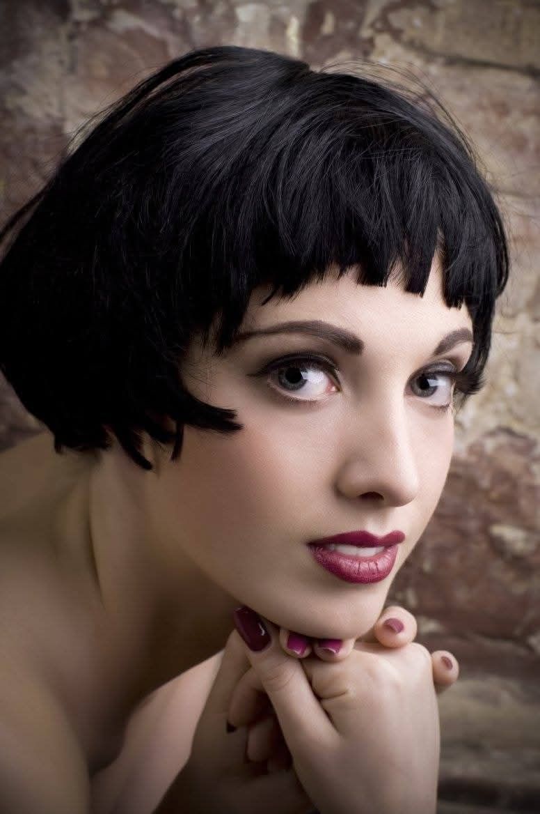 Ritratto di una persona con capelli corti e neri, con il mento appoggiato sulle mani, che guarda in camera su uno sfondo con texture.