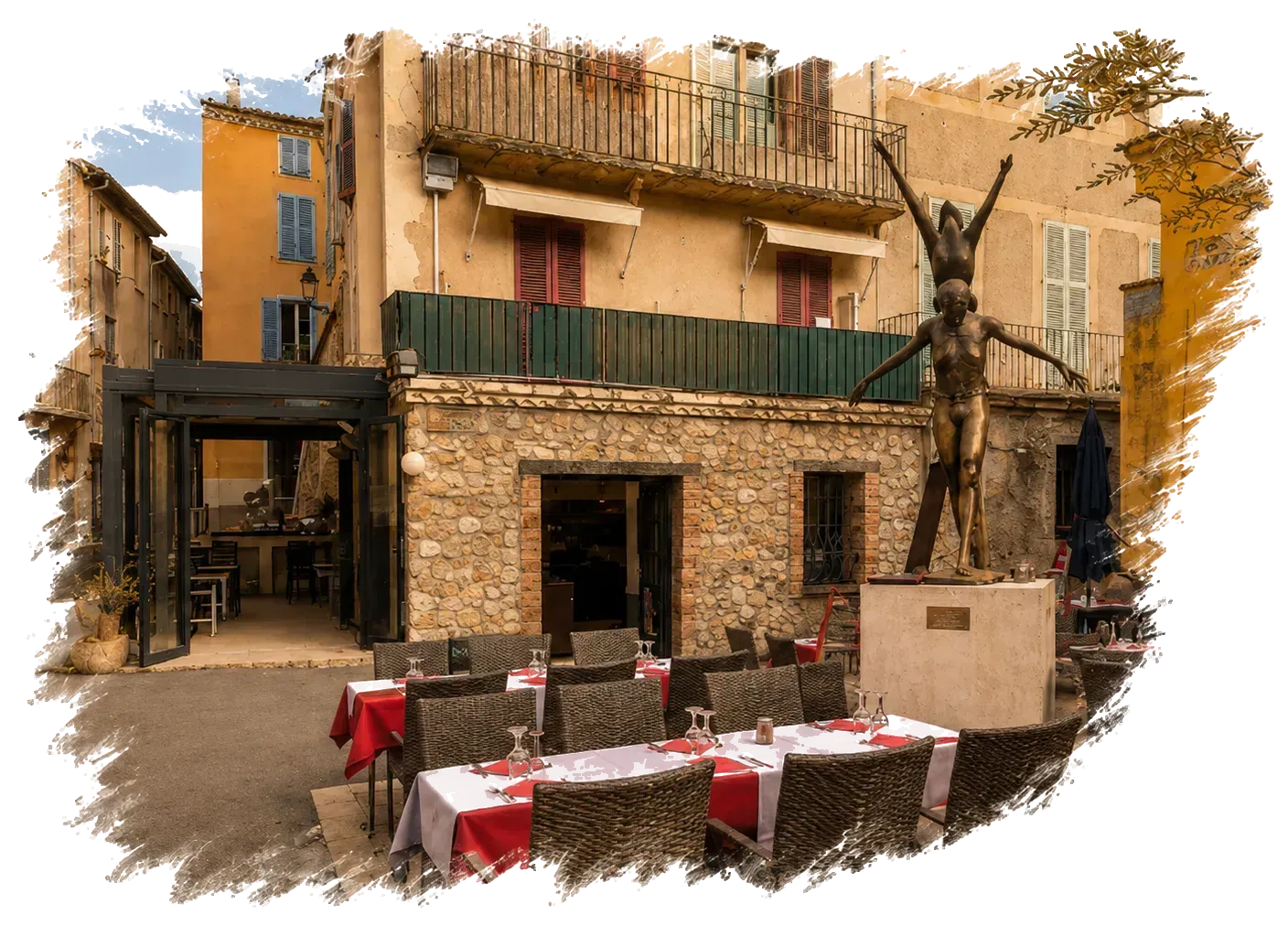 Bâtiment en pierre avec balcon vert et nappes rouges sur une terrasse extérieure