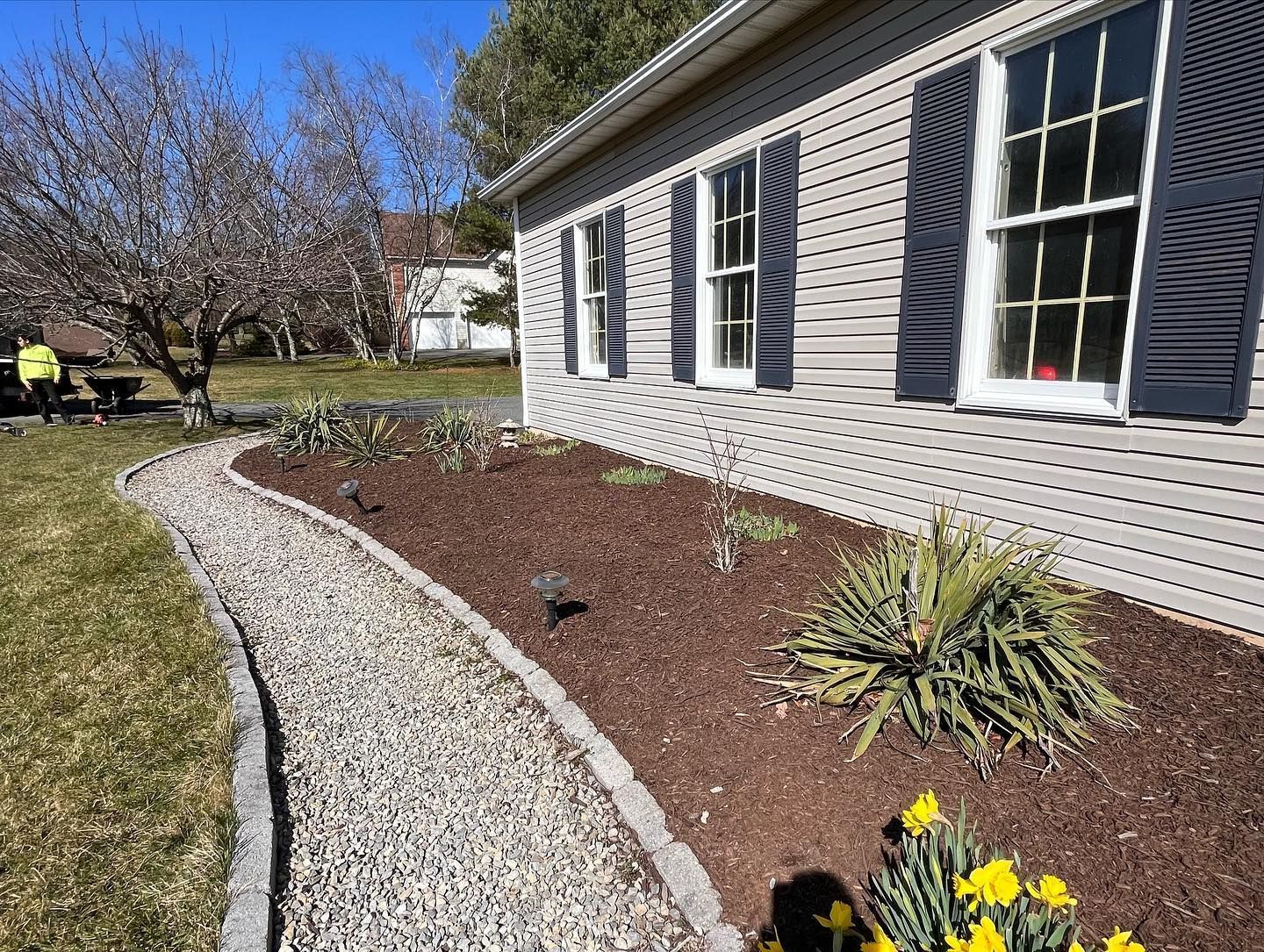 A house with a gravel path leading to it and flowers in front of it.