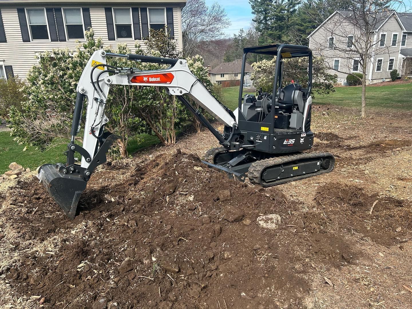 A small excavator is digging a hole in the dirt in front of a house.