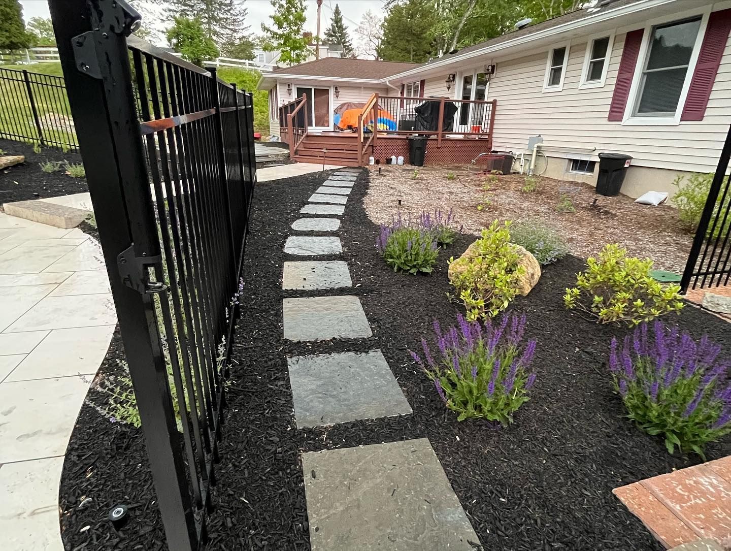 A walkway leading to a house with a fence and flowers.