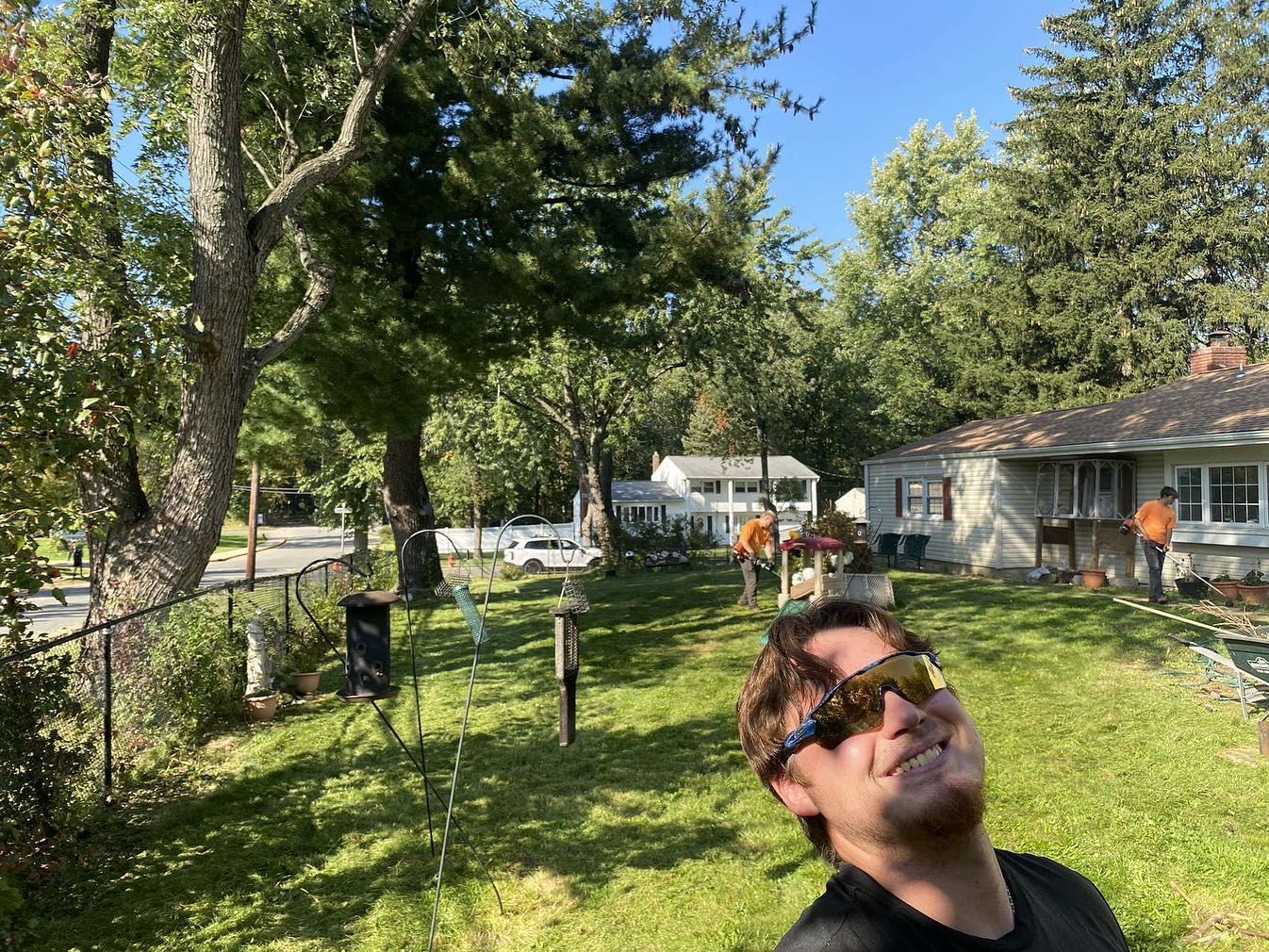 A man wearing sunglasses is standing in the grass in front of a house.