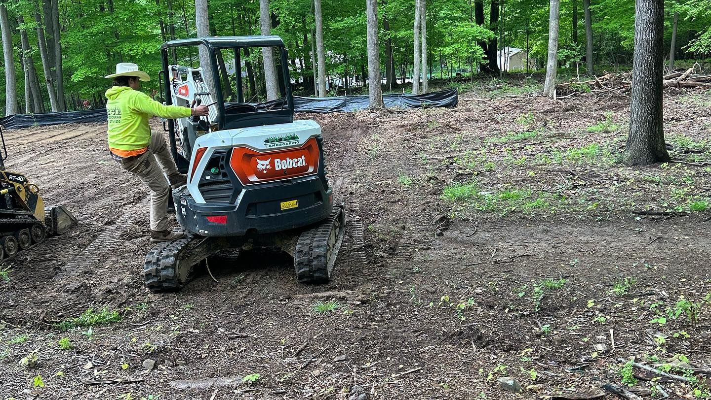 A man is standing next to a small bulldozer in the woods.