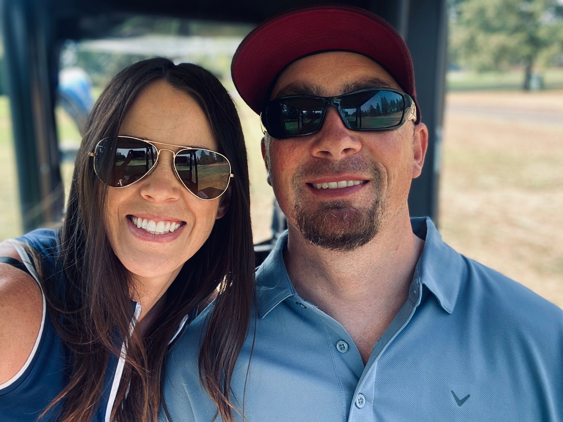 The owners of Trademark Tek in sunglasses smile at the camera while sitting in a golf cart in Medford, Oregon.