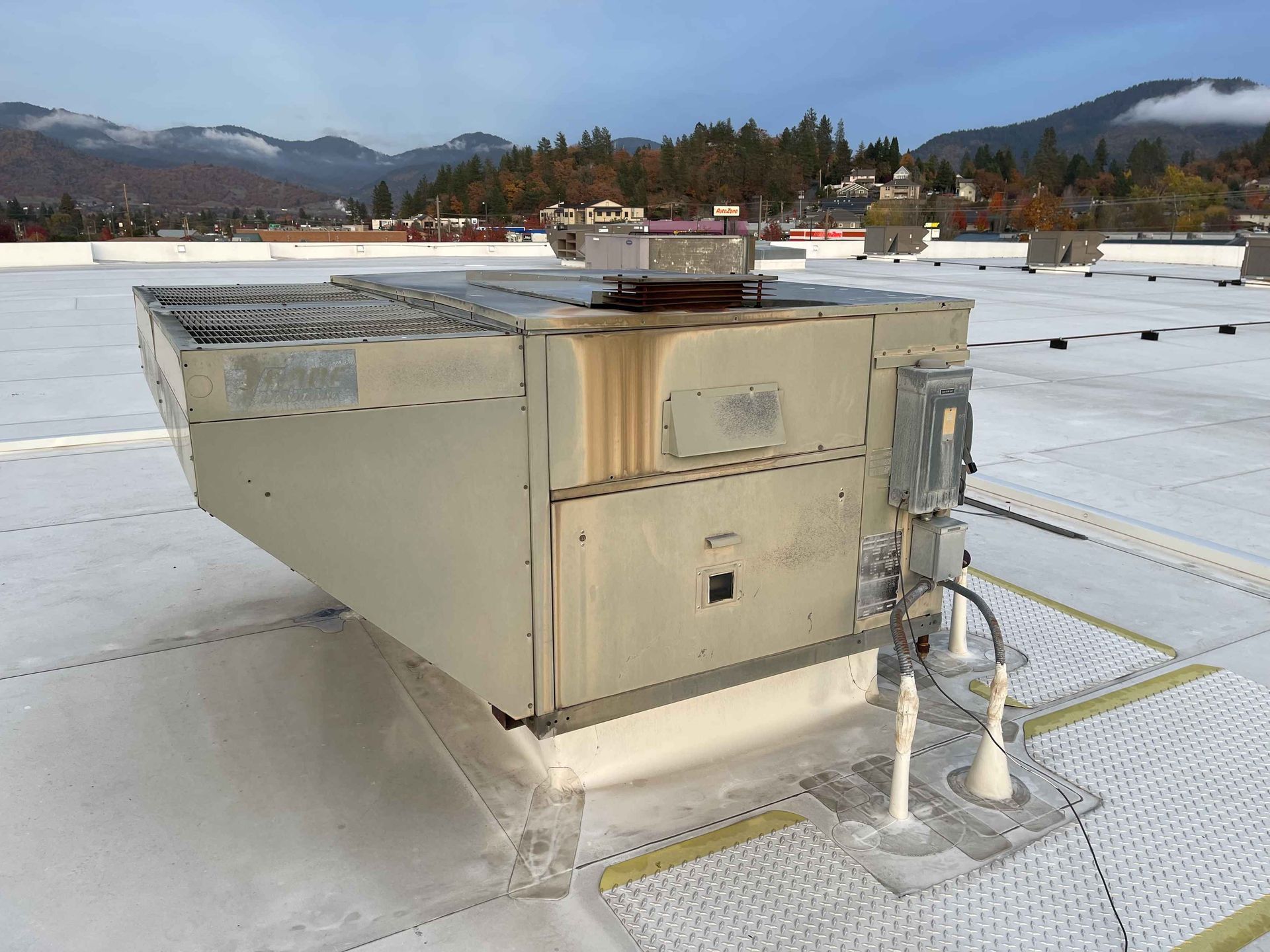 HVAC unit on a white roof, with mountain and town in the background.