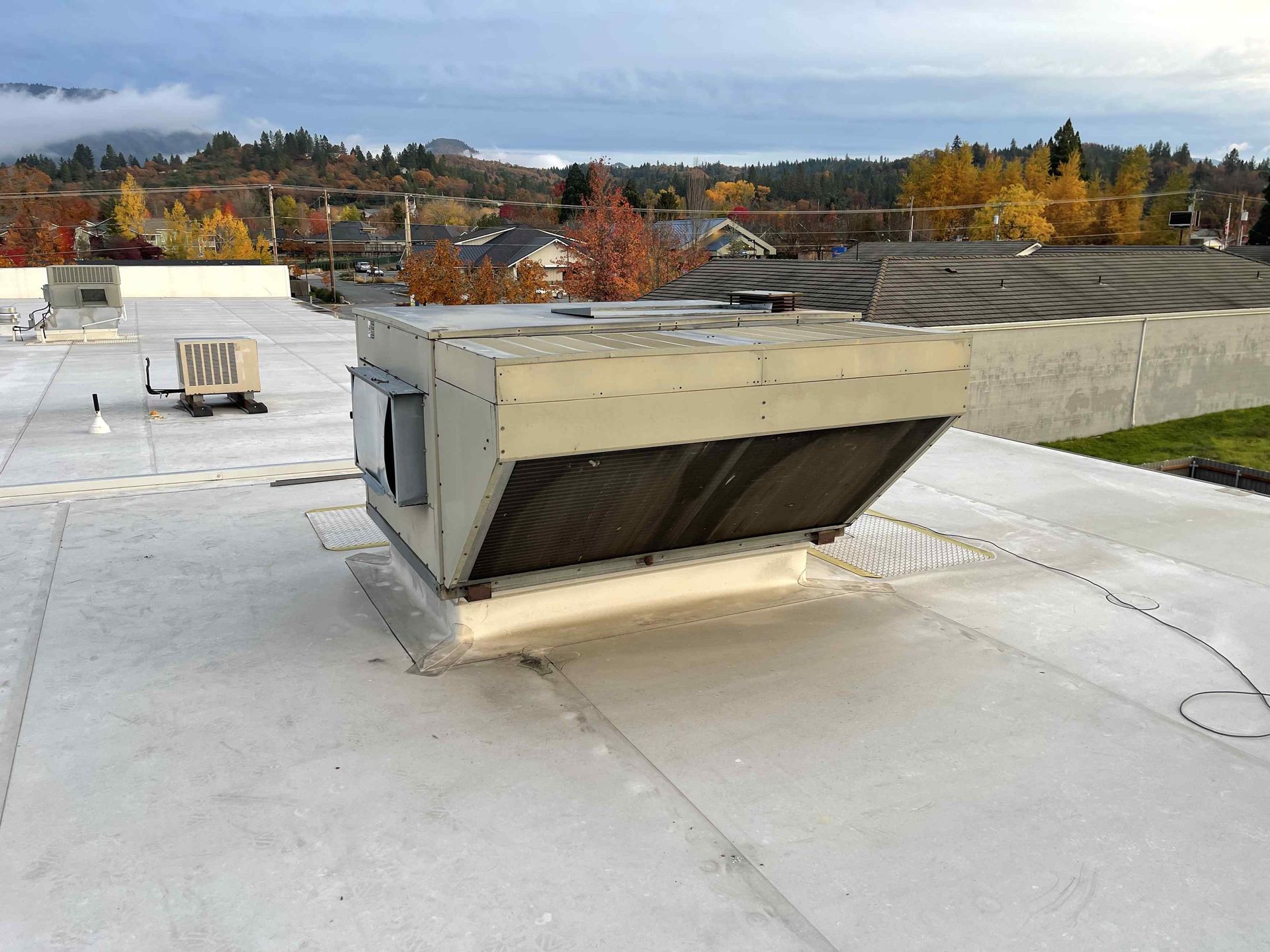 Large HVAC unit on a flat white roof with a distant fall landscape background of Medford, Oregon.
