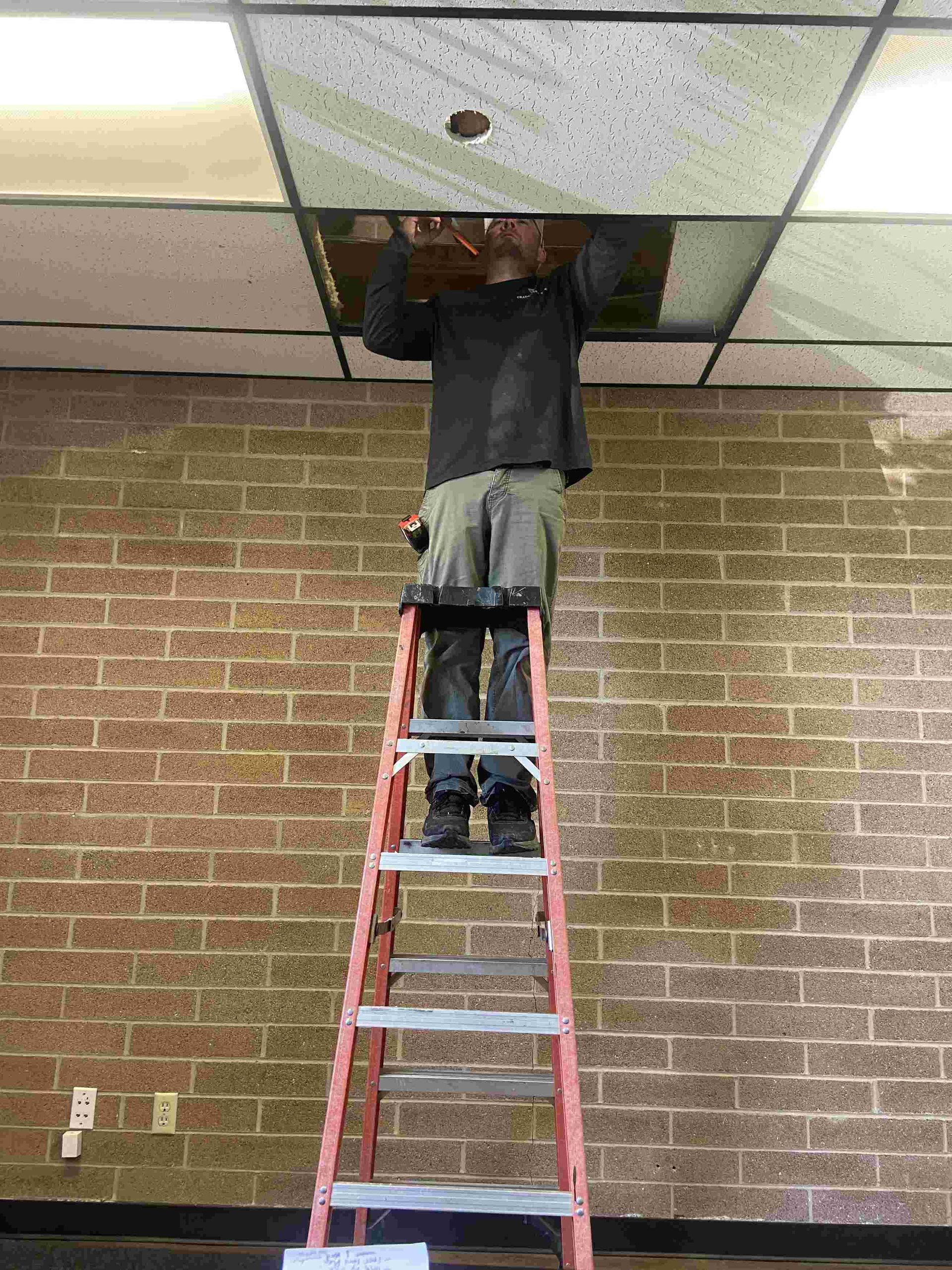 Person on ladder inspecting an HVAC system in a ceiling of a commercial building in Medford, Oregon.
