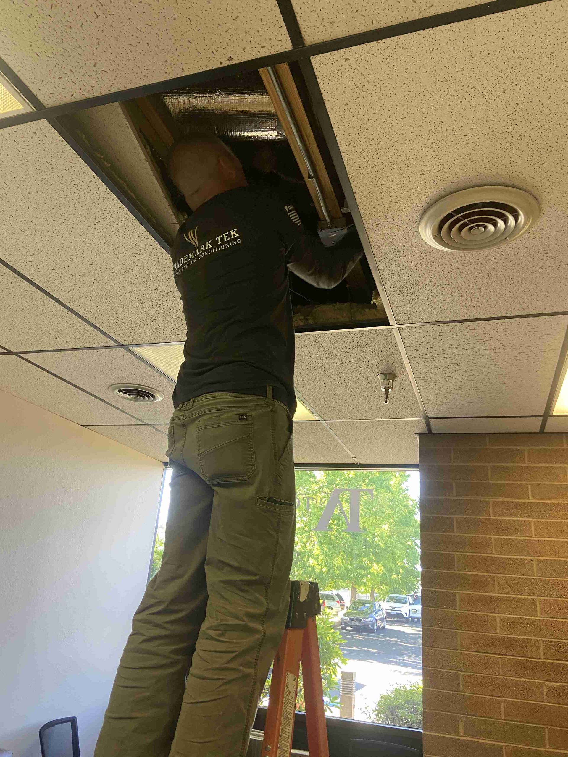 Man on a ladder installing HVAC ducting in an office in Southern Oregon.
